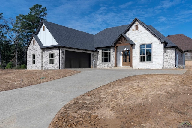 view of front of home with a shingled roof, board and batten siding, a garage, stone siding, and driveway