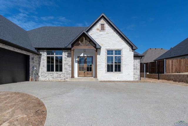 view of front facade with a shingled roof, fence, stone siding, french doors, and driveway