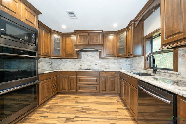 kitchen featuring light stone counters, built in microwave, sink, dishwasher, and light hardwood / wood-style floors