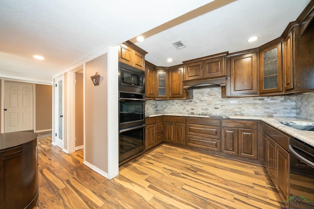 kitchen featuring decorative backsplash, light hardwood / wood-style flooring, light stone counters, and black appliances