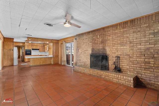 unfurnished living room with a brick fireplace, brick wall, visible vents, and a ceiling fan