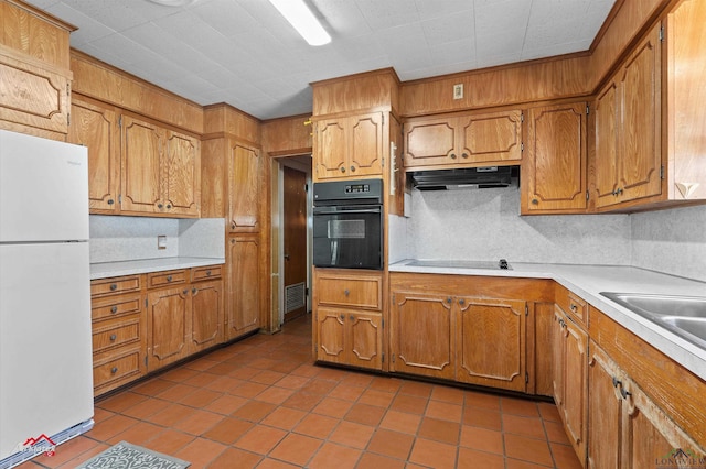 kitchen featuring brown cabinetry, light countertops, under cabinet range hood, and black appliances