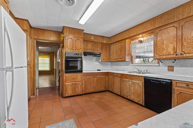 kitchen featuring light countertops, brown cabinetry, a sink, wood walls, and black appliances