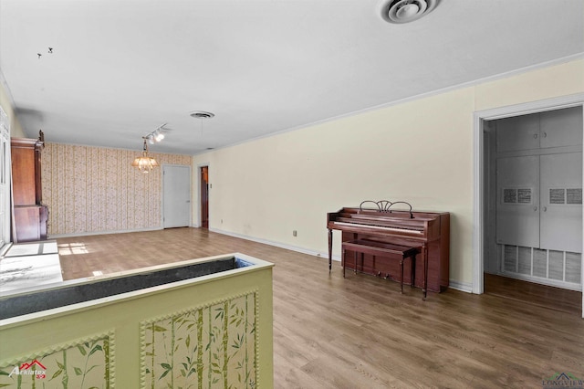 interior space featuring wallpapered walls, baseboards, wood finished floors, crown molding, and a notable chandelier