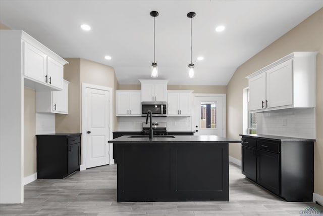 kitchen with lofted ceiling, white cabinets, appliances with stainless steel finishes, and a center island with sink