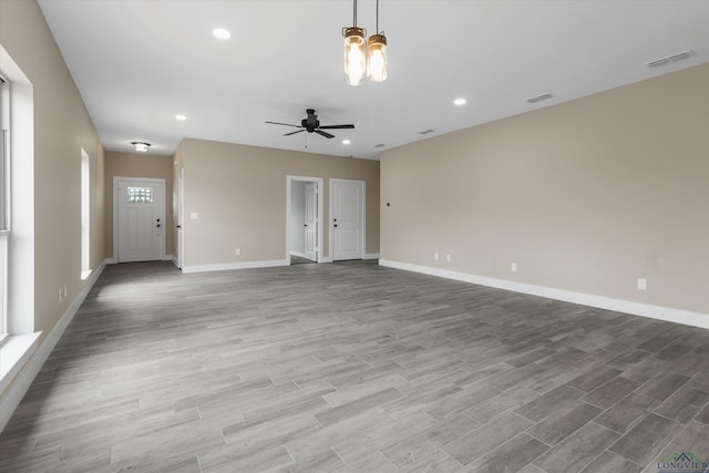 unfurnished living room with ceiling fan with notable chandelier and light hardwood / wood-style floors