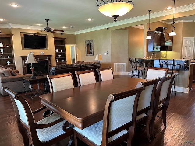 23196 Jeb Cir, Frankston, TX 75763 - dining space with a ceiling fan, dark wood-style flooring, a fireplace, ornamental molding, and recessed lighting