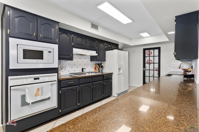 kitchen featuring white appliances, backsplash, dark stone counters, sink, and light tile patterned flooring