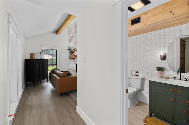 bathroom featuring toilet, vanity, lofted ceiling with beams, and wood-type flooring