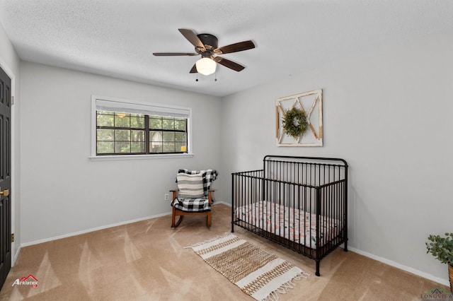 bedroom with a crib, a textured ceiling, light colored carpet, and ceiling fan