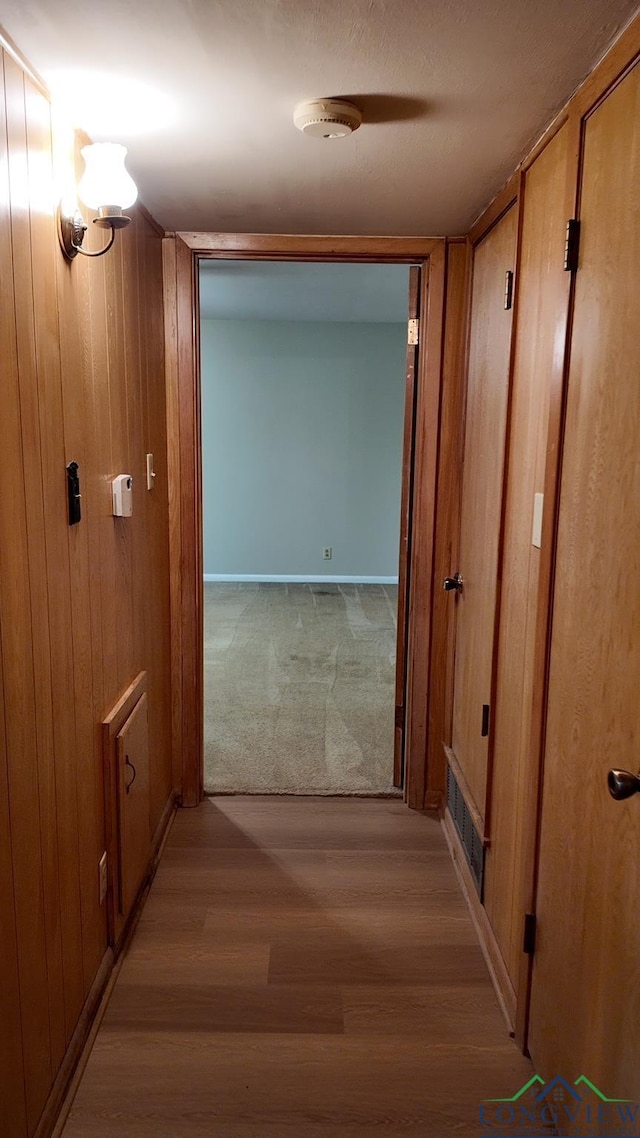 hall with light wood-type flooring and wooden walls