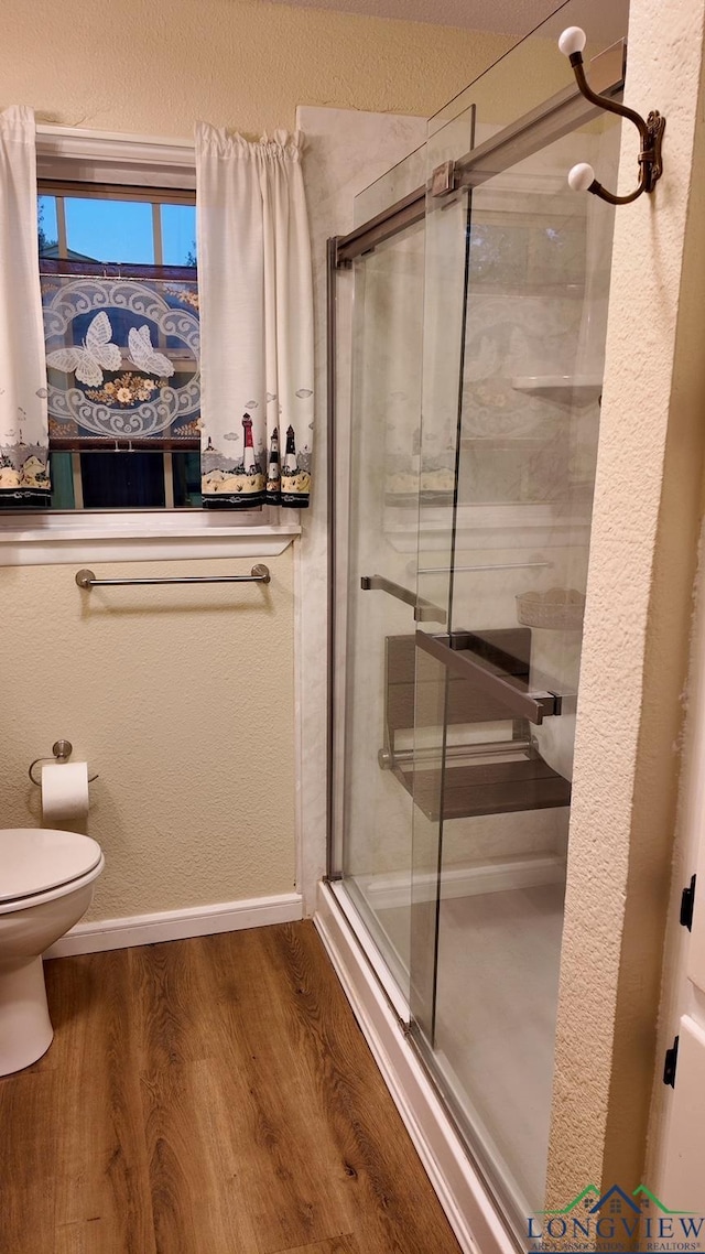 bathroom featuring toilet, a shower with door, and hardwood / wood-style flooring