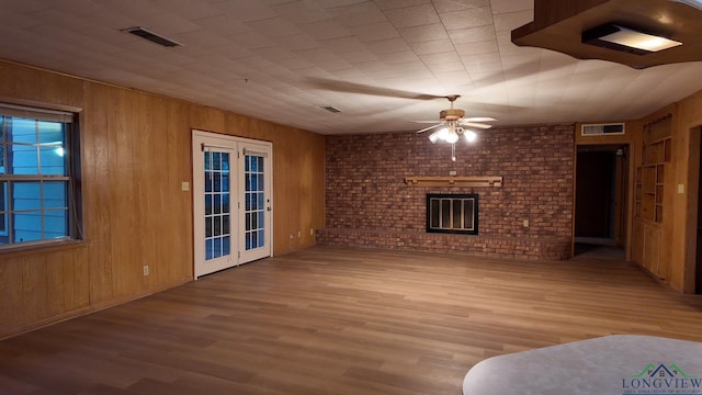 unfurnished living room featuring a brick fireplace, ceiling fan, wood walls, and french doors