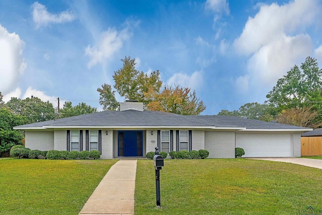 ranch-style home featuring a chimney, concrete driveway, an attached garage, brick siding, and a front yard