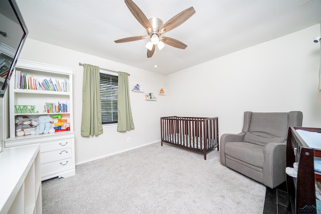 bedroom with a textured ceiling, ceiling fan, a crib, and light carpet