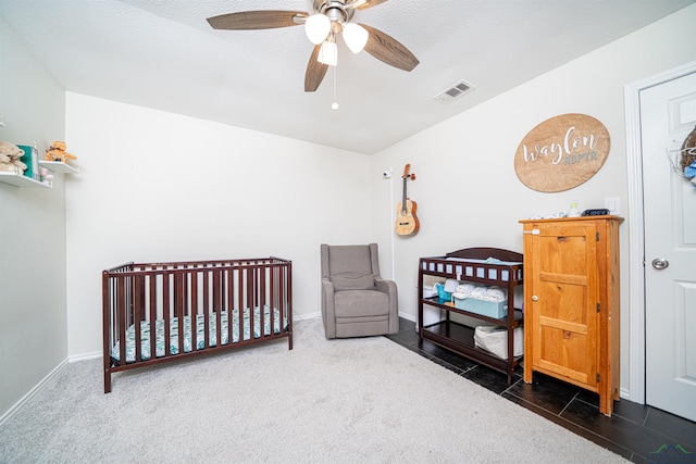 bedroom with a crib, dark carpet, and ceiling fan