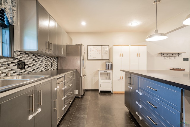 kitchen featuring sink, decorative backsplash, blue cabinetry, decorative light fixtures, and stainless steel refrigerator