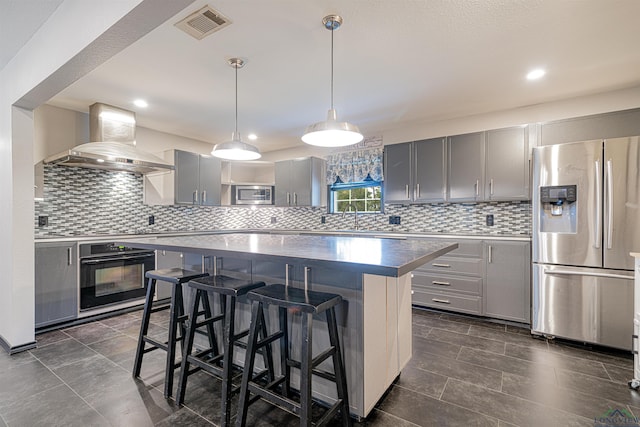 kitchen featuring wall chimney exhaust hood, stainless steel appliances, pendant lighting, a breakfast bar, and a kitchen island