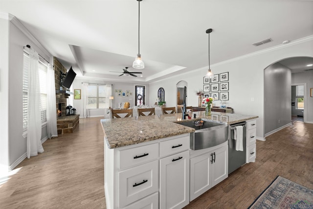 kitchen featuring dishwasher, white cabinetry, a kitchen island with sink, light stone countertops, and a raised ceiling