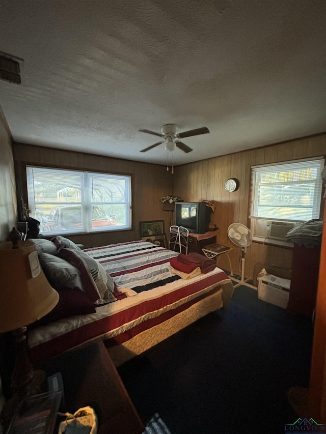 bedroom with ceiling fan, wooden walls, carpet floors, and a textured ceiling