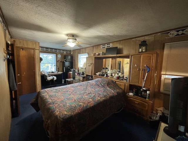 carpeted bedroom with a textured ceiling, ceiling fan, and wood walls