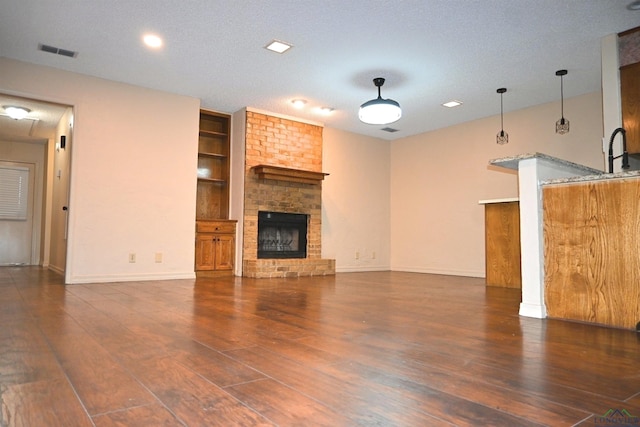 811 Georgia Ln, Longview, TX 75604 - unfurnished living room with wood finished floors, a brick fireplace, built in shelves, and a textured ceiling