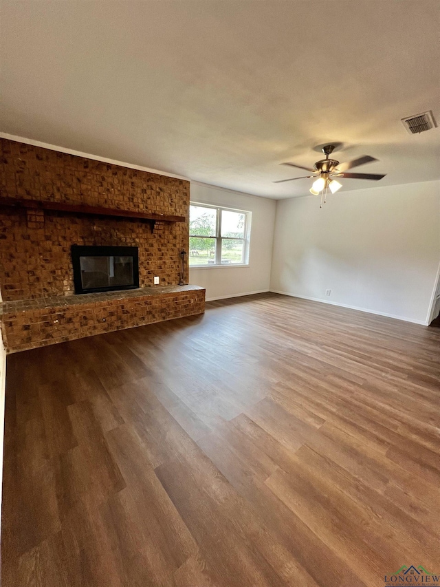 unfurnished living room with wood-type flooring, a brick fireplace, and ceiling fan