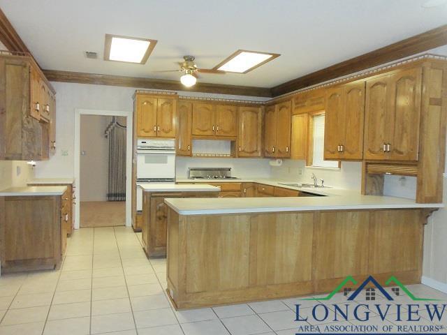 404 Moccasin Trl, Kilgore, TX 75662 - kitchen with a peninsula, brown cabinetry, light countertops, light tile patterned floors, and a sink