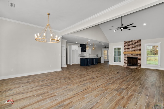 unfurnished living room with a brick fireplace, ornamental molding, ceiling fan with notable chandelier, vaulted ceiling, and sink