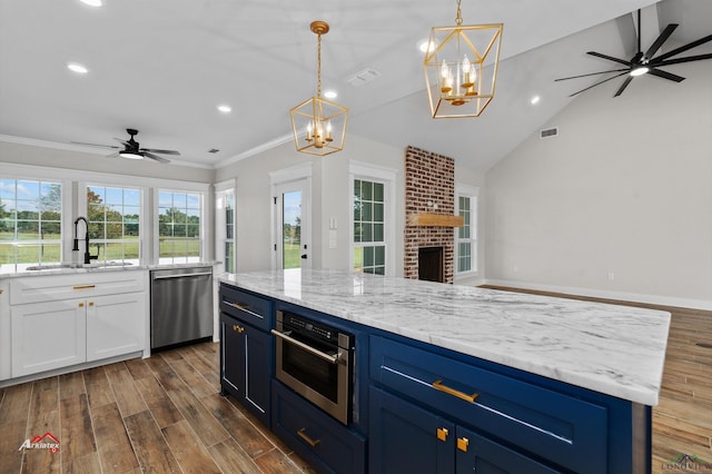 kitchen with appliances with stainless steel finishes, a brick fireplace, ceiling fan with notable chandelier, sink, and a center island