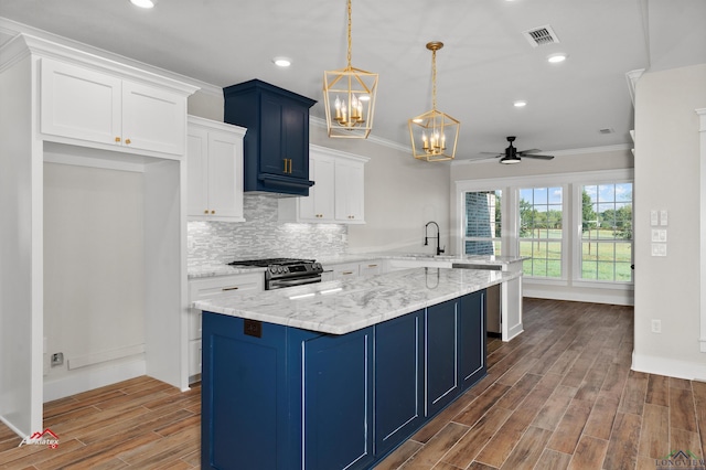 kitchen with kitchen peninsula, ceiling fan with notable chandelier, white cabinets, stainless steel gas stove, and hanging light fixtures