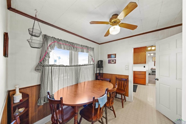 dining area with crown molding, ceiling fan, and wooden walls