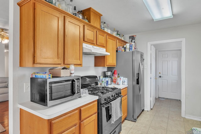 kitchen with stainless steel appliances, light tile patterned flooring, brown cabinets, light countertops, and under cabinet range hood