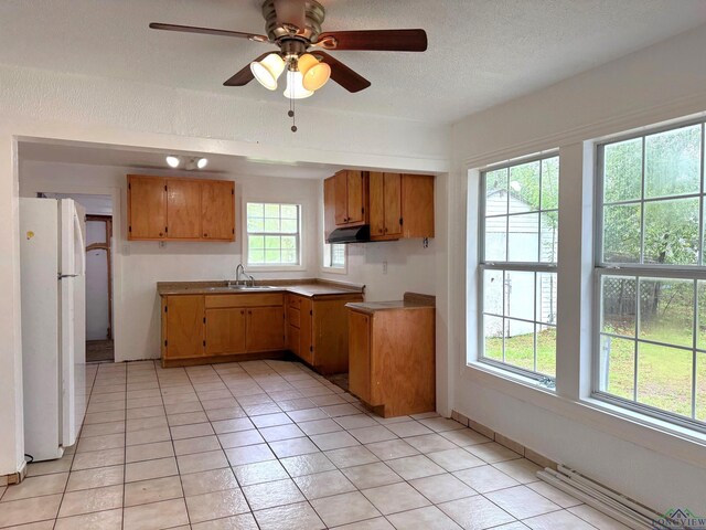 308 E 14th St, Mount Pleasant, TX 75455 - kitchen featuring a textured ceiling, under cabinet range hood, a sink, brown cabinetry, and freestanding refrigerator