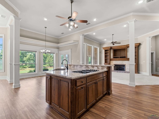 kitchen featuring ornamental molding, a kitchen island with sink, stainless steel gas cooktop, sink, and a fireplace