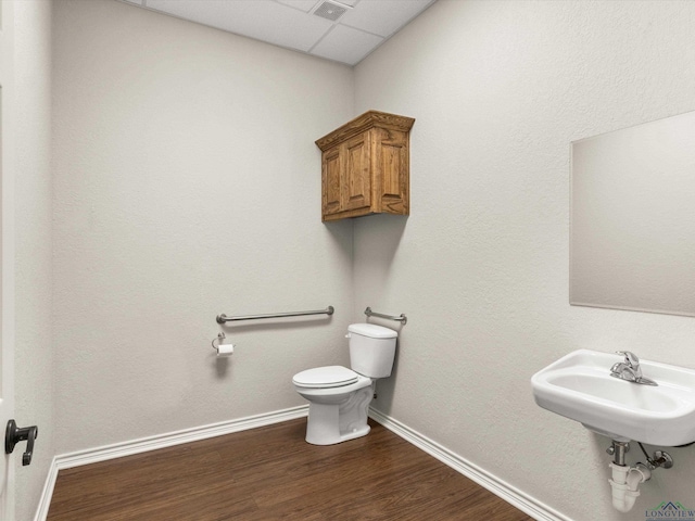 bathroom featuring hardwood / wood-style flooring, a drop ceiling, toilet, and sink