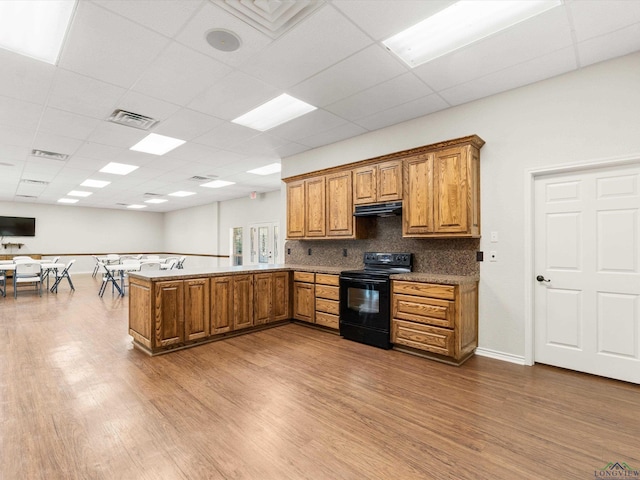 kitchen featuring kitchen peninsula, tasteful backsplash, a drop ceiling, electric range, and hardwood / wood-style flooring