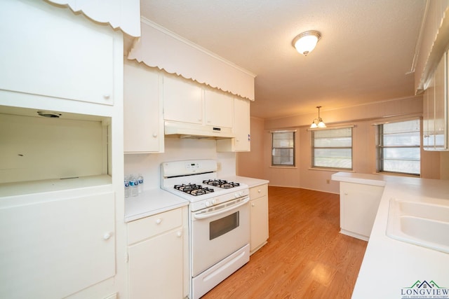 kitchen with white gas range, white cabinetry, sink, hanging light fixtures, and light wood-type flooring