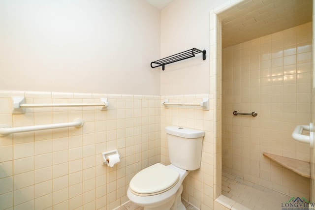 bathroom featuring a tile shower, toilet, and tile walls