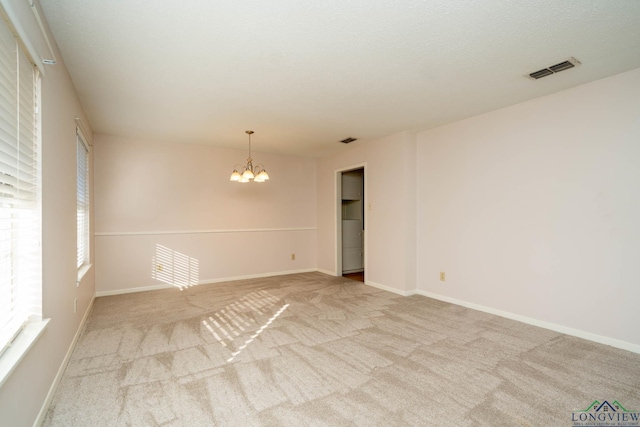 unfurnished room featuring light carpet and an inviting chandelier