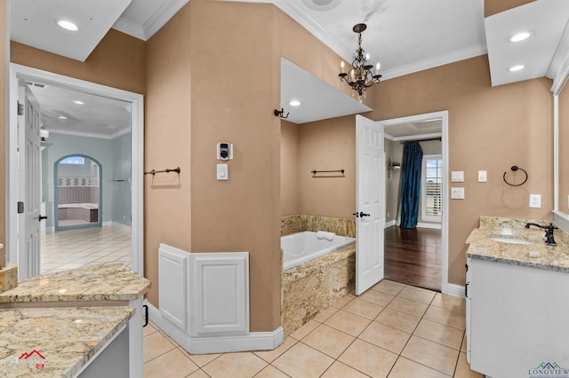 bathroom with tiled tub, crown molding, vanity, and a notable chandelier