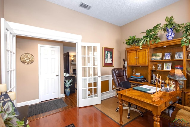 home office with a textured ceiling, visible vents, wood finished floors, and french doors