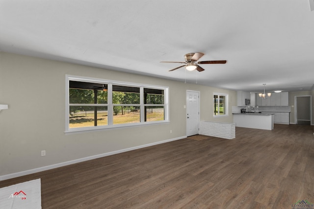 unfurnished living room with a wealth of natural light, dark hardwood / wood-style flooring, and ceiling fan with notable chandelier