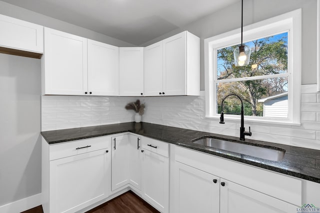 kitchen with white cabinetry, sink, tasteful backsplash, dark stone countertops, and pendant lighting