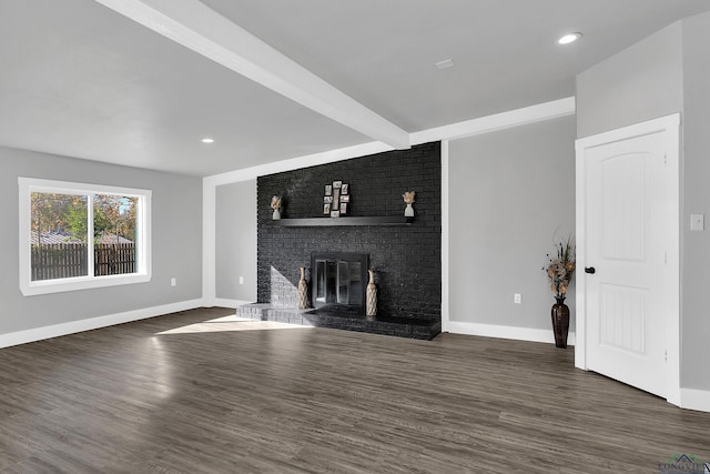 unfurnished living room featuring beam ceiling, dark wood-type flooring, and a brick fireplace