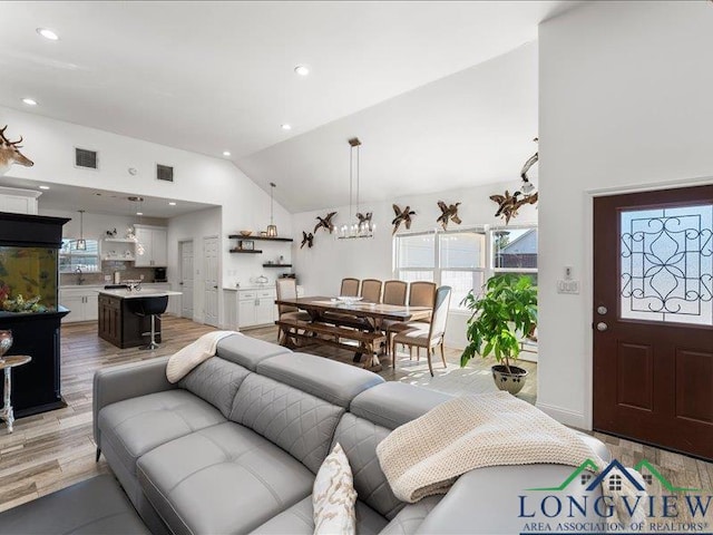 living room featuring light hardwood / wood-style floors, lofted ceiling, and an inviting chandelier