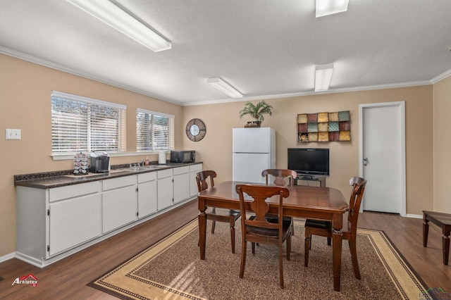 dining area with a textured ceiling, sink, crown molding, and dark wood-type flooring