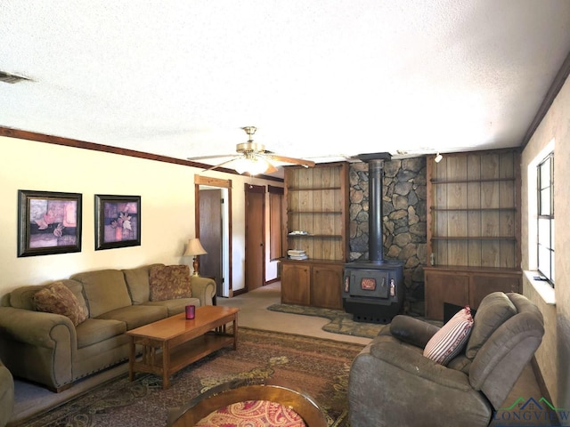 living room with ornamental molding, a textured ceiling, ceiling fan, wooden walls, and a wood stove