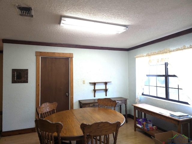 dining area featuring a textured ceiling, light wood-type flooring, and crown molding