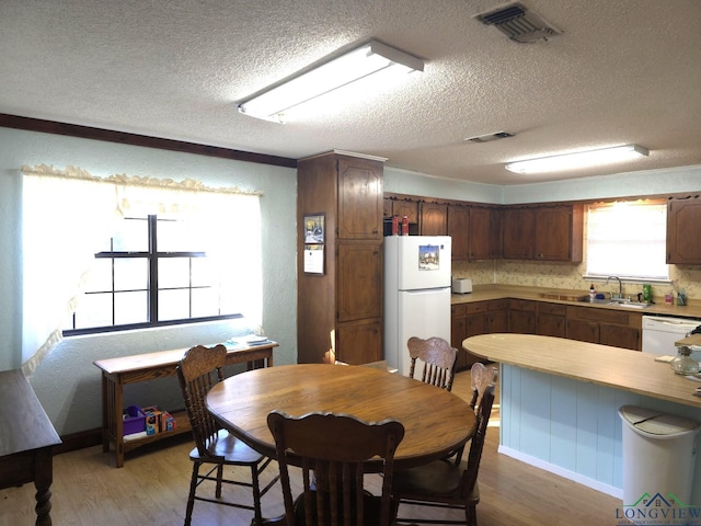 dining room with a textured ceiling, sink, and light hardwood / wood-style flooring